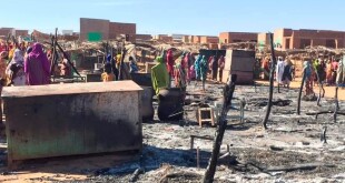 Residents of a refugee camp gather around the burned remains of makeshift structures, in Genena, Sudan.   (Organization for the General Coordination of Camps for Displaced and Refugees / AP)